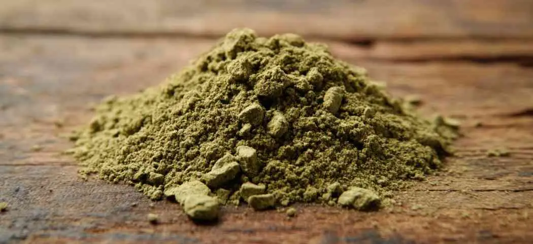 Pile of green kratom powder on a wooden table